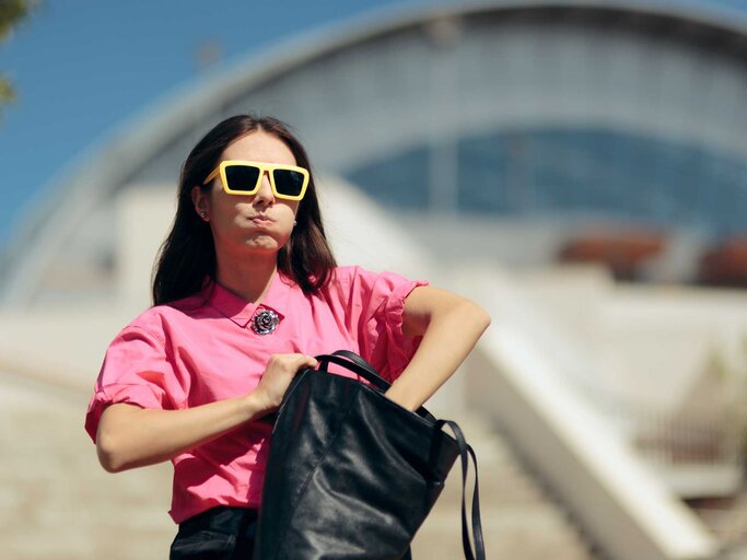 Frau mit gelber Sonnenbrille sucht genervt in ihrer großen Handtasche | © Getty Images/nicoletaionescu