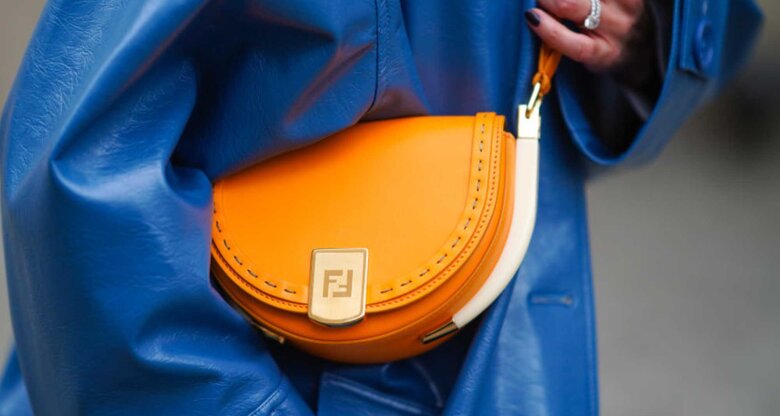 Frau trägt blauen Ledermantel und orangefarbene Halfmoon Bag | © Getty Images/Edward Berthelot 