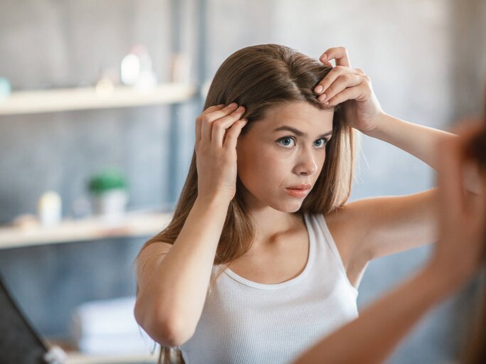 Frau begutachtet ihre Kopfhaut im Spiegel | © gettyimages.de / Prostock-Studio