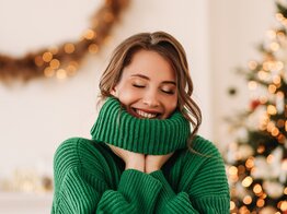 Eine Frau ist glücklich und steht lächelnd vor einem Christbaum | © GettyImages/Elizaveta Starkova