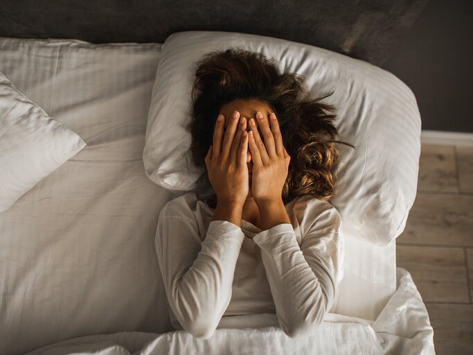 Eine Frau liegt im Bett, bedeckt das Gesicht mit ihren Händen und möchte das Gedankenkarussell stoppen! | © GettyImages/Oleg Breslavtsev