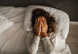 Eine Frau liegt im Bett, bedeckt das Gesicht mit ihren Händen und möchte das Gedankenkarussell stoppen! | © GettyImages/Oleg Breslavtsev