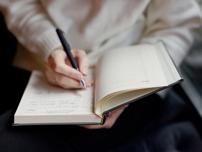 Hände einer Frau, die ihre Gedanken in ein Buch schreibt. | © GettyImages/Oksana Nazarchuk M