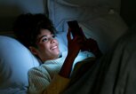 Eine Frau liegt im Bett und ist am Handy. | © GettyImages/Hispanolistic