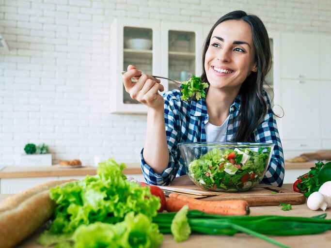 Junge Frau lacht und isst einen Salat | © iStock | Povozniuk
