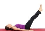 Frau liegt mit dem Rücken auf einer Yoga-Matte und hebt ihre Beine gerade an. | © iStock | DenizA