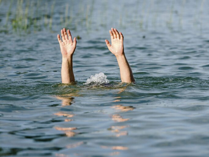 Hände ragen aus dem Wasser, um eine ertrinkende Person darzustellen | © iStock.com / kulkann
