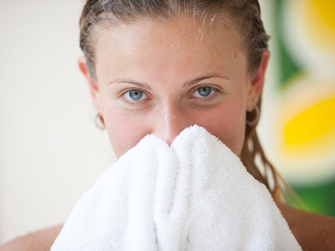 Frau trocknet sich das Gesicht mit einem Handtuch ab | © iStock.com / ShotShare