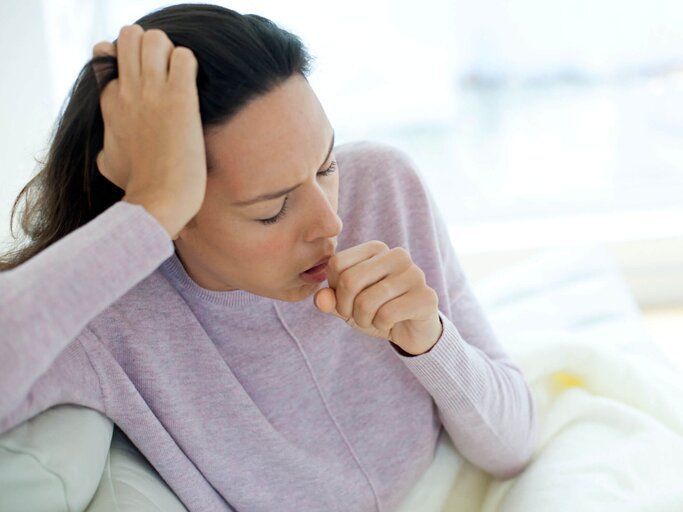 Frau sitzt mit einer Grippe auf der Couch und hustet. | © gettyimages.de / Science Photo Library