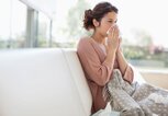 Frau sitzt mit einer Decke auf der Couch und putzt sich wegen Schnupfen die Nase. | © gettyimages.de / Paul Bradbury