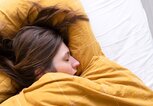 Frau liegt mit Gliederschmerzen im Bett und hat geschlossene Augen. | © gettyimages.de / Roos Koole