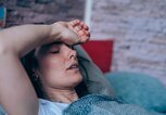 Frau liegt mit Fieber und geschlossenen Augen im Bett und hält ihre Stirn. | © gettyimages.de / VioletaStoimenova