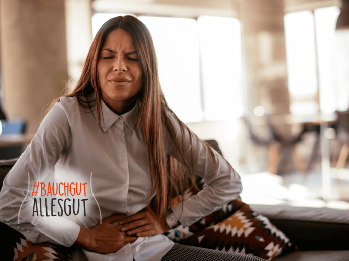Frau sitzt mit Magenschmerzen auf der Couch. | © iStock.com / Milos Dimic